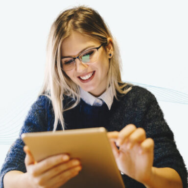 A smiling woman wearing glasses holds a tablet and interacts with the screen.