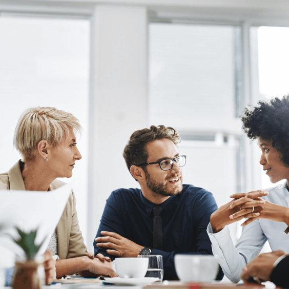 Three people conversing while seated at a meeting table.