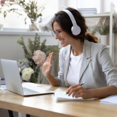 Smiling woman waving to participants in an online meeting.