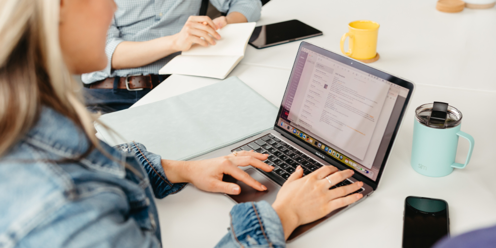 Photo of two people working, one at a laptop and the other taking notes.