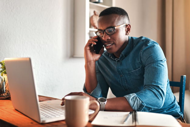 Un homme parle sur son portable tout en travaillant sur son ordinateur.