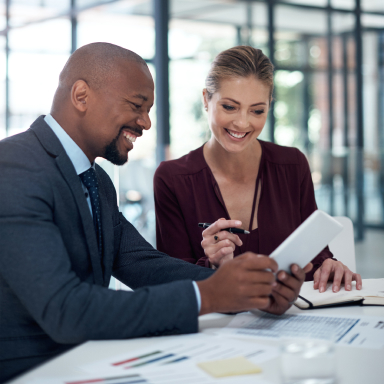 Two smiling people looking at something on a tablet.