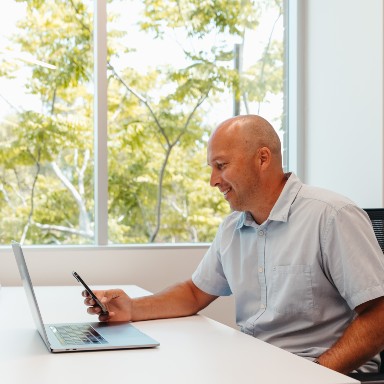 Smiling man seated at his desk and looking at his mobile.