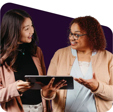 Two smiling women in conversation about something on a notebook.