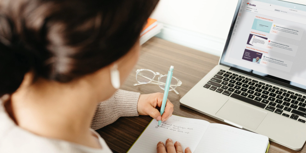 A person seated at desk writing on a tablet.