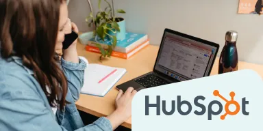 HubSpot logo + an image of woman talking on a mobile while seated at a work station.