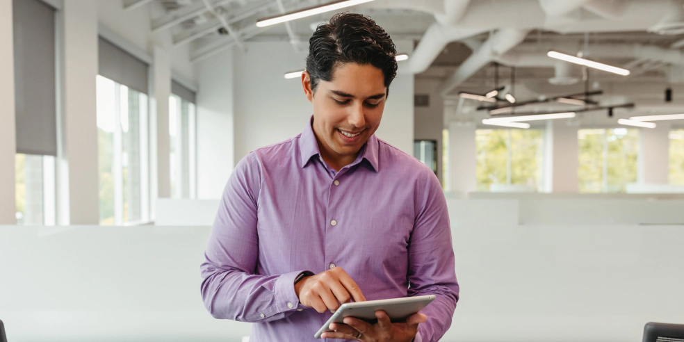 A man wearing purple shirt looks at tablet screen.