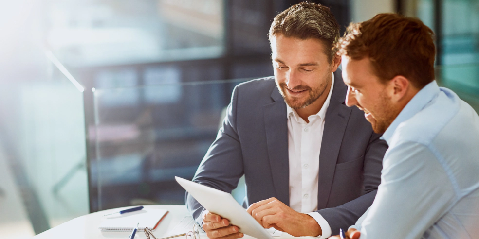 A financial advisor seated next to a client while pointing to his laptop.